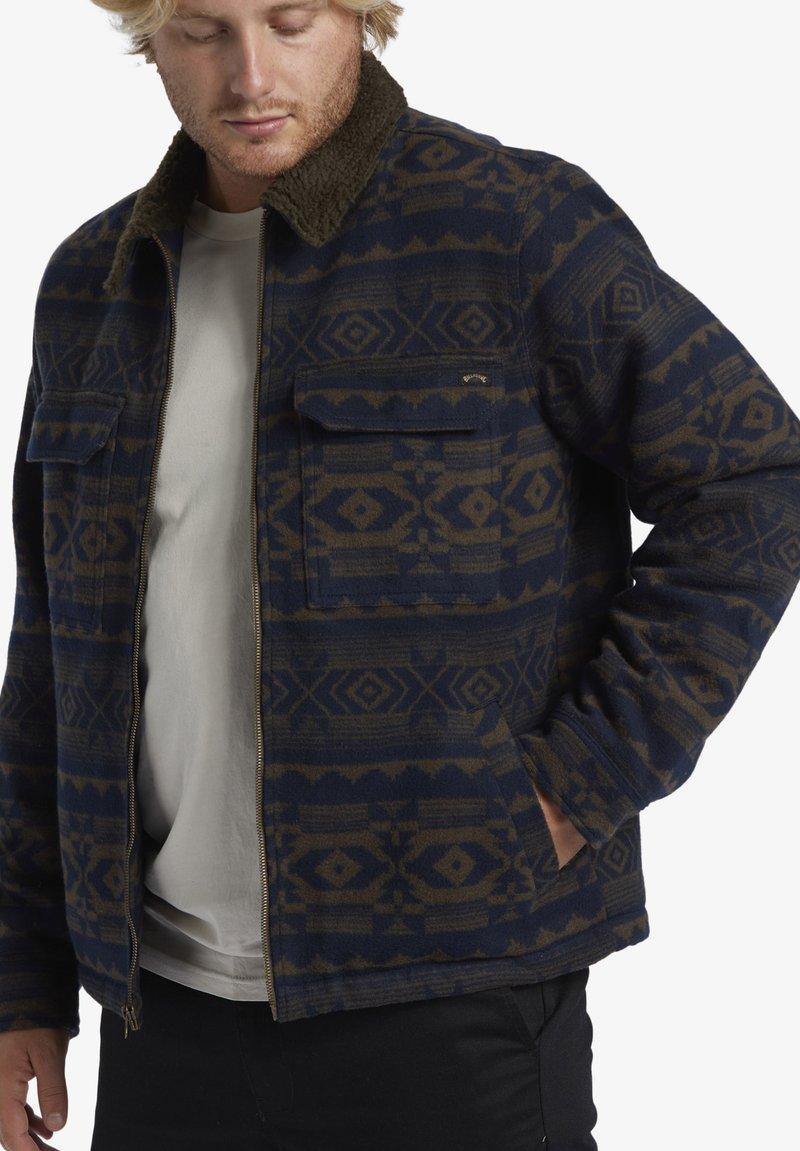 Bluish jacket with a geometric pattern in dark brown. Features a zip front, two chest pockets, and a contrasting fuzzy collar.