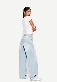 Lyseblå vidde denimjeans, parret med en tætsiddende hvid t-shirt. Glat tekstur, afslappet design med baglommer.