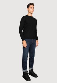 Suéter negro de mangas largas, jeans azules y zapatillas de caña alta negras. El suéter tiene cuello redondo, los jeans son ajustados con puños enrollados.