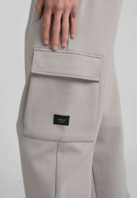 Pantaloni cargo beige con tasca laterale e etichetta nera Replay. Realizzati in tessuto morbido e strutturato. Design semplice con accenti minimi.
