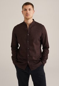 Cămașă button-up de culoare maro închis, cu guler mandarin, mâneci lungi și o textură fină. Prezintă nasturi pe toată lungimea frontului și o croială lejeră.