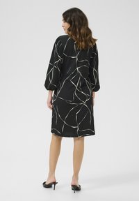 Robe noire avec des lignes abstraites blanches, dotée de manches bouffantes longues et d'une coupe droite. Tissu lisse avec un ourlet au genou.