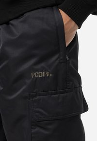 Black cargo pants made of a smooth, lightweight material. Features include a front pocket with embossed "PGDR." logo and stitched detailing.