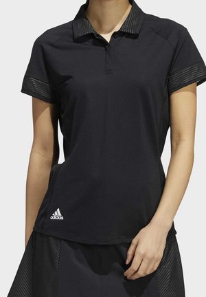 Polo noir à manches courtes avec des détails en mesh au niveau du col et des manches, porté avec une jupe assortie, arborant un logo blanc Adidas près de l’ourlet.