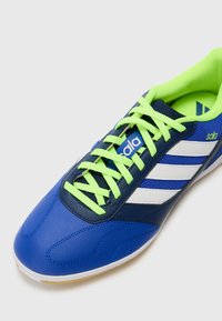Blauwe synthetische sportschoen met witte strepen, groene veters en een gepolsterde kraag. Beschikt over een gestructureerde bovenkant en rubberen zool.