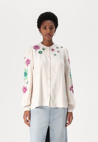 Kremfarget skjorte med fargerik blomsterbroderi på ermene, med knappestolpe foran og myk, lett stoff. Kombinert med en denimskjørt.