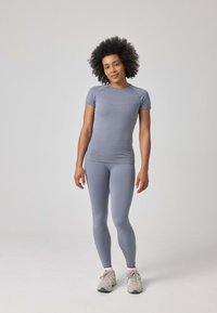 Top atletico grigio chiaro e leggings in un design aderente, realizzati in un materiale morbido ed elastico; abbinati a sneakers di colore chiaro.