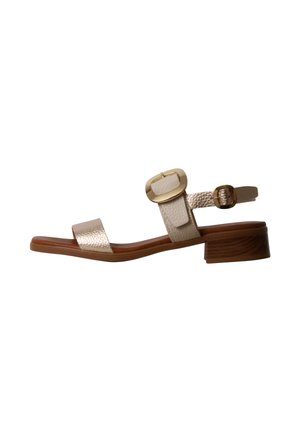 Beige sandal med åben tå, lav træblokhæl, teksturerede stropper og guldfarvet spændelukning på ankelremmen.