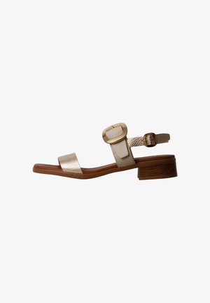 Beige sandal med åben tå, lav træblokhæl, teksturerede stropper og guldfarvet spændelukning på ankelremmen.