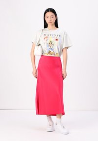T-shirt graphique gris avec un design de Matisse, associé à une jupe midi satin rose vif et des baskets blanches avec des chaussettes épaisses.