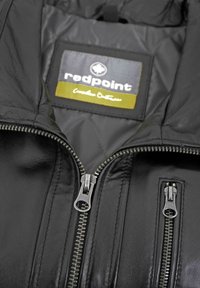 Schwarze Lederjacke mit einem gesteppte Futter, doppelten Front-Reißverschlüssen und einem Etikett mit der Aufschrift "redpoint", das ein Logo und Farbakzente trägt.