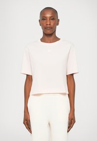 Tricou scurt de culoare roz deschis, fabricat dintr-un material moale, având un guler rotund și mâneci scurte, asortat cu pantaloni de culoare deschisă.