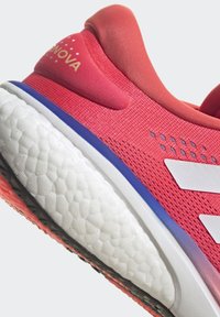 Zapatilla deportiva rosa con parte superior de malla, acentos blancos y suela texturizada. Cuenta con un collar acolchado y detalles de diseño únicos.