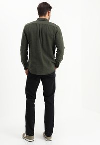 Grön, texturerad skjorta med knappkrage, kombinerad med svarta byxor. Avslappnad passform med rundad nederdel och kontrasterande sömmar.