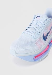 Shoe atlético azul claro com parte superior em malha, acentos rosa e uma almofada de ar visível na sola. Detalhado com um logo azul escuro.