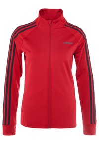 Chaqueta roja con cremallera, fabricada en tejido suave, que presenta acentos en negro con tres franjas en las mangas y un cuello alto. Logo sutil en el frente.