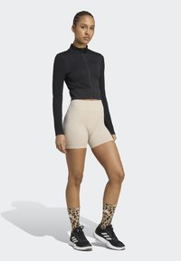 Czarny crop top na suwak, beżowe szorty kompresyjne i czarne buty sportowe. Skarpetki w leoparda do kolan. Gładka tekstura materiału.