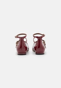 Burgunderfarbene Lacklederschuhe mit runder Zehenform, knöchelhohem Riemen und goldener Schnalle. Flache Sohle und Ausschnittdesign an der Ferse.