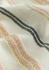 Close-up van gestructureerde witte stof met geweven roze, beige en zwarte horizontale strepen die een zacht, golvend patroon vormen.