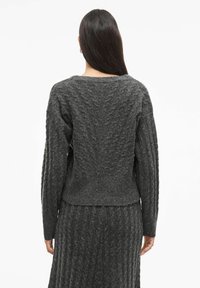 Maglione grigio lavorato a maglia con un motivo strutturato, caratterizzato da maniche lunghe e una vestibilità rilassata, indossato con una gonna coordinata a trama strutturata.