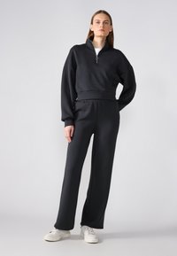 Black, cropped sweatshirt with a high neckline and zip closure, paired with matching loose-fit pants. Cotton blend fabric; minimalistic design.