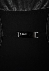 Acercamiento de una tela negra con un cierre metálico que presenta el nombre de la marca "casall" en letras blancas.