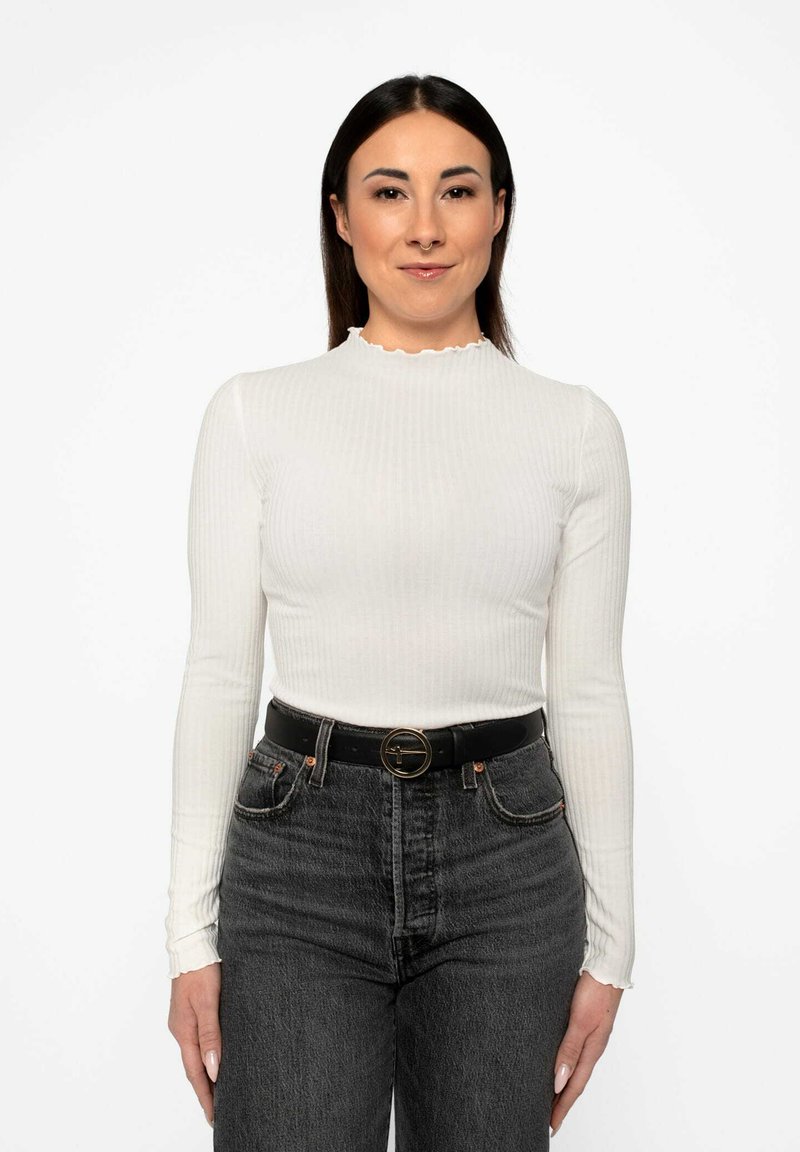 Hvid ribbet langærmet top med scalloped halsudskæring, parret med høj talje sorte jeans og et sort bælte med en cirkulær spænde.