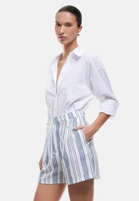 Witte button-up shirt gecombineerd met wit en blauw gestreepte hoge taille shorts met zijzakken en een gestructureerde stof.