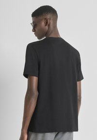 Camiseta de algodón negra con mangas cortas y un corte relajado. La parte de atrás presenta un diseño liso y un cuello redondo, sin acentos notables.