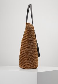 Brązowa pleciona torebka o trójkątnym kształcie, z fakturowaną powierzchnią i gładkim czarnym paskiem. Z boku ozdobiona frędzlem.