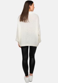 Witte gebreide oversized trui met een gemêleerd patroon, lange mouwen; gecombineerd met zwarte glanzende leggings en witte sneakers.