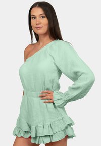 Mintgroene one-shoulder jurk van textuurstof met ruches aan de zoom en mouwen, met een aansluitende taille.