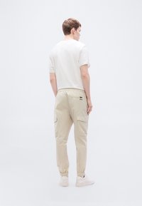 Μπεζ παντελόνι cargo με ελαστικά τελειώματα και πλαϊνές τσέπες, σε συνδυασμό με απλό λευκό κοντομάνικο πουκάμισο. Μινιμαλιστικός σχεδιασμός, χωρίς σχέδια.