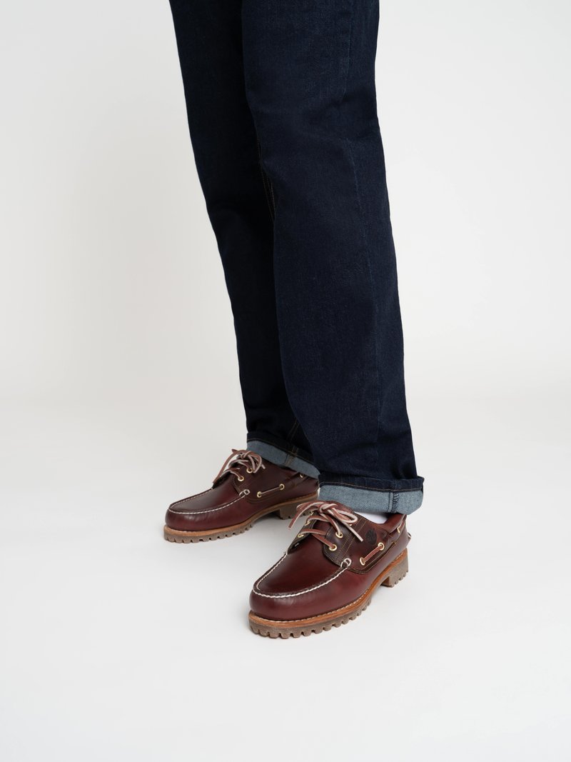 Chaussures en cuir marron avec des coutures blanches et des œillets en métal. Semelle en caoutchouc épaisse avec traction. Associées à un jean en denim noir roulotté.
