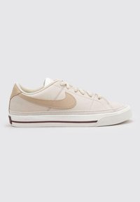 Zapatilla beige con un upper texturizado, el swoosh de Nike en tono marrón claro, suela blanca y una raya burdeos. Punta redondeada y diseño minimalista.