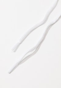 Lacets blancs avec embouts en plastique sur fond blanc, montrant un gros plan de la texture et des extrémités des lacets.