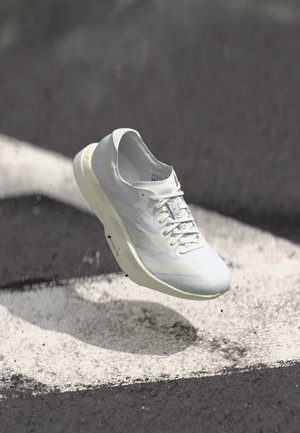 Vit sportskor svävande över asfalt med vita målade linjer, kastar skugga och små skräp runt sulan.