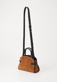 Geantă mini din suede maro cu o formă structurată, accente din piele neagră, două mânere superioare și o curea lungă ajustabilă.