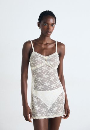 Rochie de noapte din dantelă, de culoare crem transparentă, cu un model floral. Dispune de bretele subțiri și margini volan, având un detaliu sub formă de cheie la decolteu.
