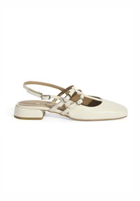 Cream-colored slingback shoes with a pointed toe, glossy patent leather, small block heel, and crisscross strap design.