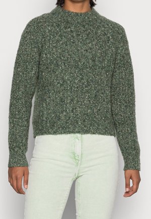 Grüner, strukturierten Strickpullover mit hohem Kragen und langen Ärmeln, kombiniert mit hellgrünen, gerippten Hosen.