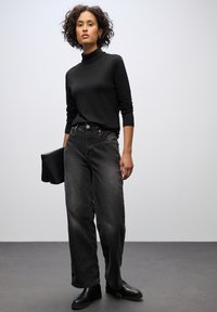 Maglione nero a collo alto, jeans larghi grigi scuri a vita alta, stivaletti neri alla caviglia, con una pochette nera. Texture liscia, vestibilità casual.