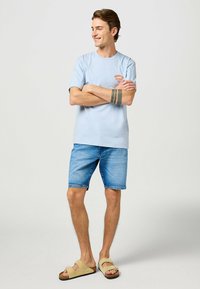 Svetlo modra bombažna majica s krožnim izrezom in potiskom na levem prsnem delu, v kombinaciji z modrimi jeans kratkimi hlačami in bež natikači. Obleka za sproščeno priložnost.