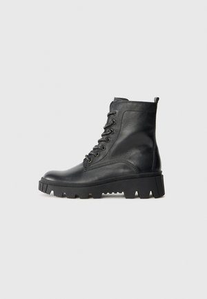 Bottines en cuir noir avec un bout arrondi, un laçage sur le devant et une semelle en caoutchouc texturée dotée de crampons proéminents pour une bonne adhérence.