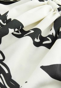 Mustvalge mustriga kangas, sileda tekstuuriga; disainis voolavad kujundid kreemikal taustal, ülaservas kergelt kortsus.