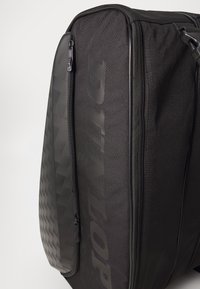 Schwarze Duffelbag mit strukturiertem Oberflächenmaterial, das ein glattes geometrisches Muster und einen großen Reißverschluss aufweist. "DUNLOP"-Logo geprägt an der Seite.