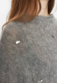 Sivkasta pletena jopica z odprtim tkanjem in dekorativnimi sijočimi dragulji. Ima okroglo ovratnico in mehak, teksturiran material.