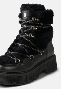 Czarne botki za kostkę z futerkiem, z teksturowaną skórzaną podstawą, z metalowymi przelotkami, plecionymi sznurówkami i grubą, żebrowaną podeszwą.