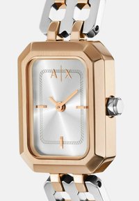 Obdĺžnikové hodinky so strieborným ciferníkom, ružovo zlatými tónmi, textúrovanými akcentmi a náramkom s prepojeniami v ružovom zlate a striebre.