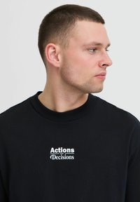 Zwarte sweatshirt met een ronde hals, voorzien van witte tekst "Acties en Beslissingen" op de borst. Glad katoen, casual pasvorm.